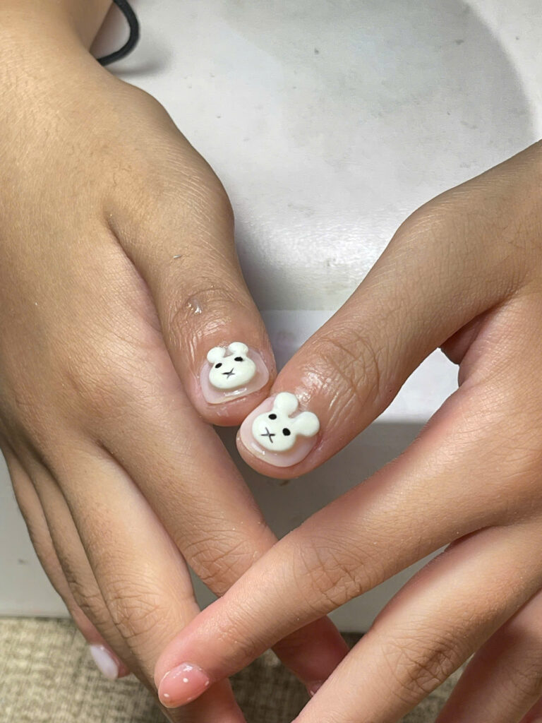 Close-up of two nails decorated with white 3D bunny charms at Art Spa 2, Hoi An