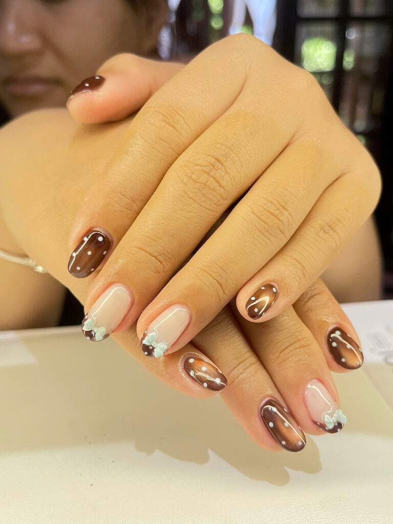 Brown cat-eye nails with white dots and mint bows at Art Spa 2, Hoi An
