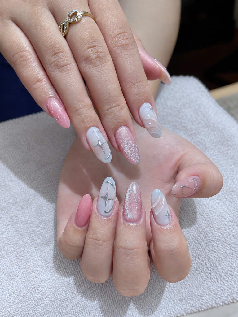 Long almond nails with silver chrome stars, glitter and a bow design at Art Spa 2, Hoi An