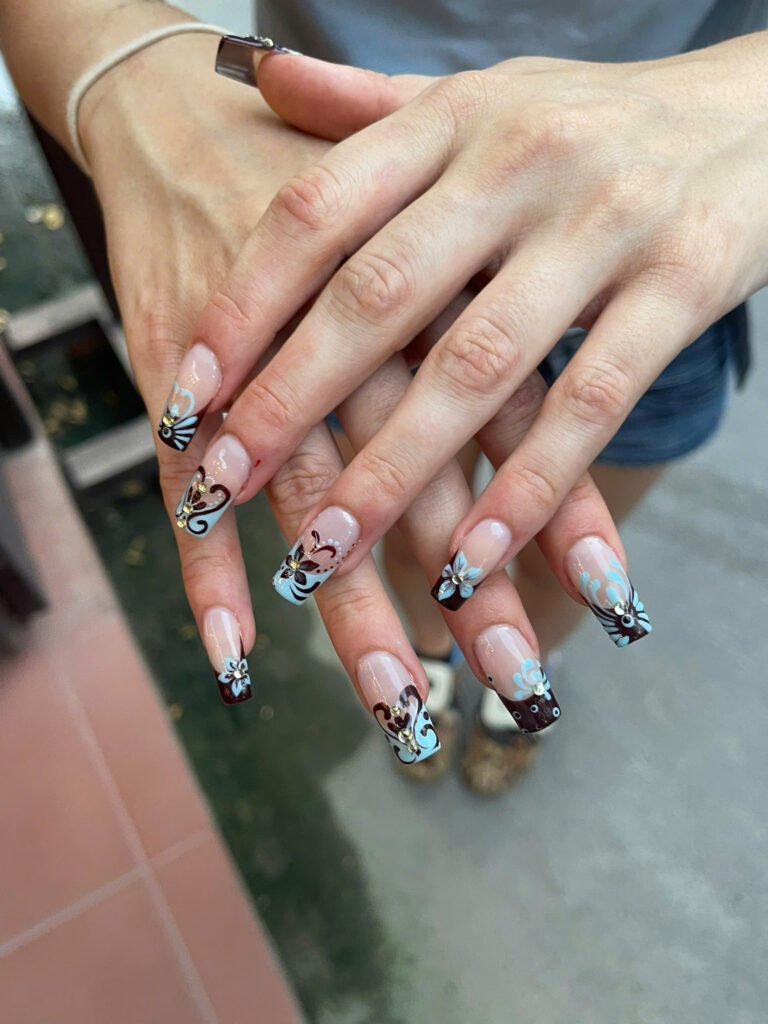 Long French tip nails with hand-painted brown and light blue flowers and rhinestones at Art Spa 2, Hoi An